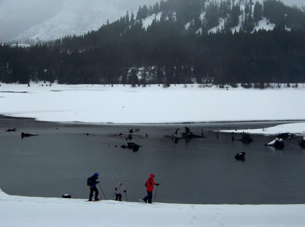 Personnes pratiquant les raquettes autour d'un lac au pied d'une montagne enneigée