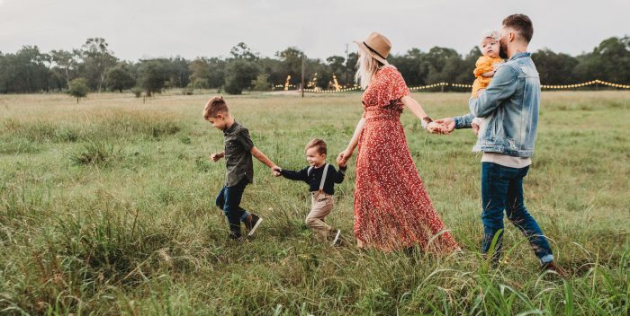 Plusieurs membres d'une famille, parents en enfants, qui courent dans un champ en se tenant par la main