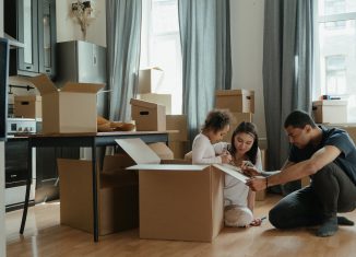 enfant assise dans un carton et qui dessine dessus avec ses parents